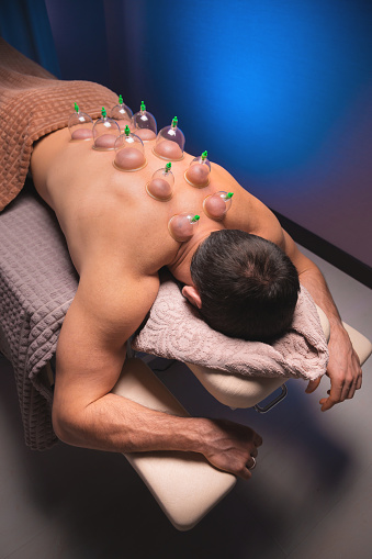 Vertical shot Relaxed young muscular man getting cupping treatment on his back lying on table.