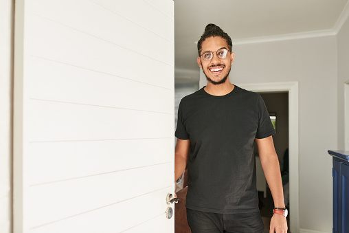 Young man opening the front door and smiling while welcoming the guest