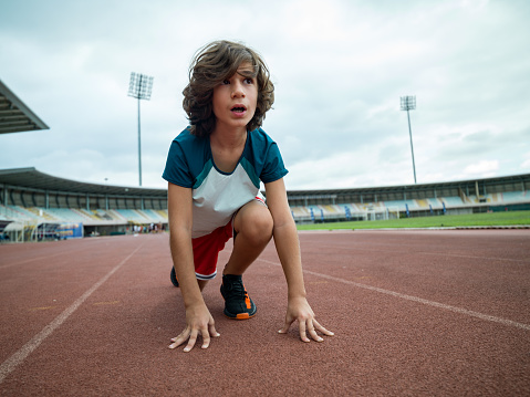 Low angle photo of boy getting ready for running in stadium. Shot under daylight with a medium format camera and a wide angle lens.