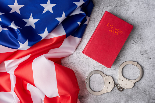 Background with United States flag next to criminal code and handcuffs on a white marble base. American judicial system. Enforcement of American rules