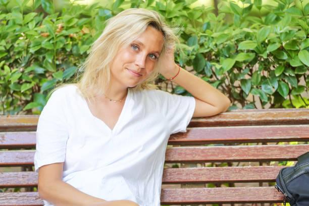 istock Woman looking at camera and smiling while sitting on a bench in a park. 1428492226