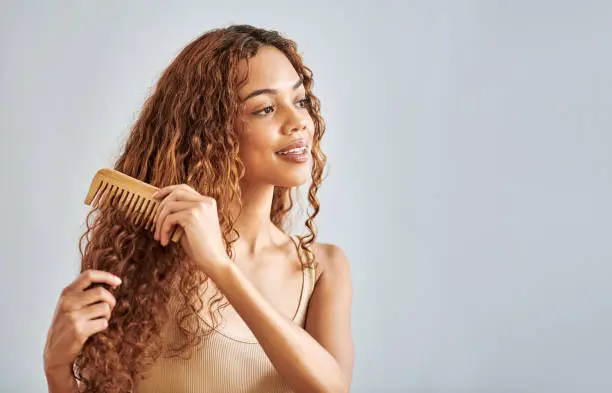Photo of Beauty, hair and brush with a woman brushing her curly hairstyle in studio on a gray background with mockup. Face, hair care and comb with an attractive young female combing her beautiful curls