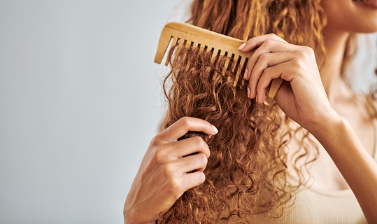 Cleaning, beauty and hair care by woman brush and style her natural, curly hair in bathroom in her home. Hygiene, frizz and damage control with female hands comb natural hair in morning routine