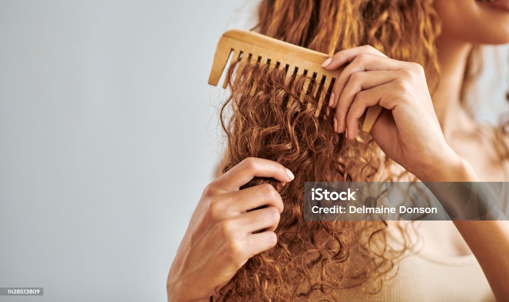 Cleaning, beauty and hair care by woman brush and style her natural, curly hair in bathroom in her home. Hygiene, frizz and damage control with female hands comb natural hair in morning routine Curly Hair Stock Photo