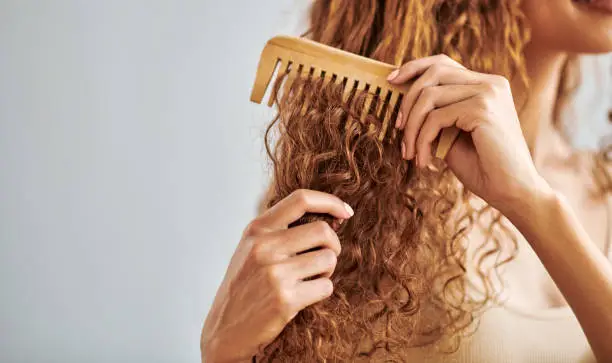 Photo of Cleaning, beauty and hair care by woman brush and style her natural, curly hair in bathroom in her home. Hygiene, frizz and damage control with female hands comb natural hair in morning routine