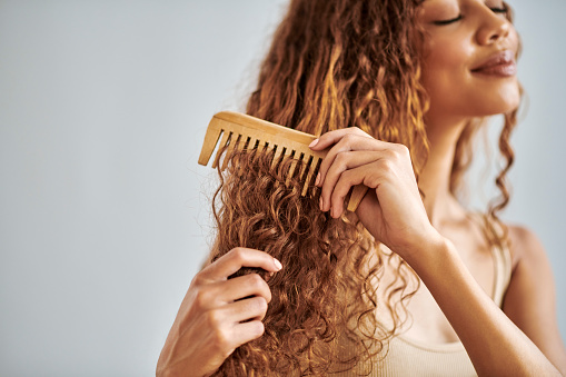 Hair care, beauty and woman brushing her curly hair with a wooden comb during her self care routine. Beautiful, young and hispanic girl combing her clean natural locks in a studio with copy space.