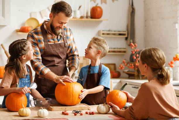 Son and dad making Jack-o-Lantern together at home, carving Halloween pumpkin