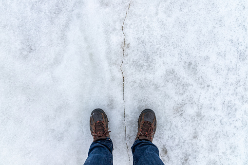 Male feet stand on a snowy ice with crack, first person view, top view
