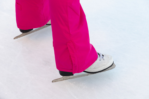 Legs of a girl in pink on skates on a white ice rink