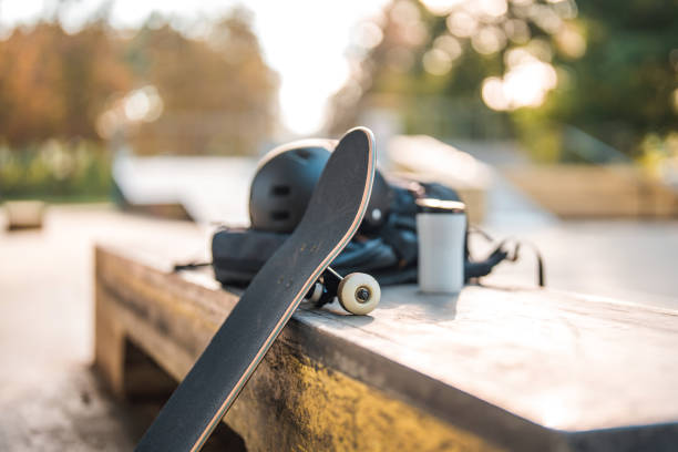 Skateboard Leaning on Curb Box With Coffee Cup and Helmet on Top of it Skateboarding equipment on and around the curb box at a skateboarding park. Portable plastic coffee cup next to a protective helmet. Focus on the board. Blurred background. skateboard stock pictures, royalty-free photos & images