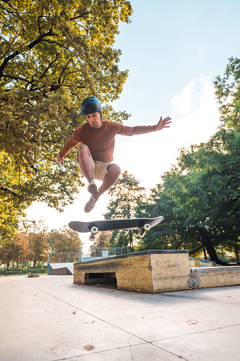 Mid adult biracial skateboarder learning   a complicated trick at an open air skate park. Low angle shot, full length image, trees and fun boxes in the background. Vertical shot.