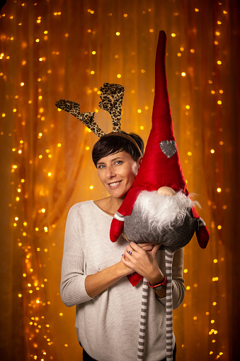 Smiling Adult woman portrait with Reindeer costume horns hugging a decorative Elf puppet