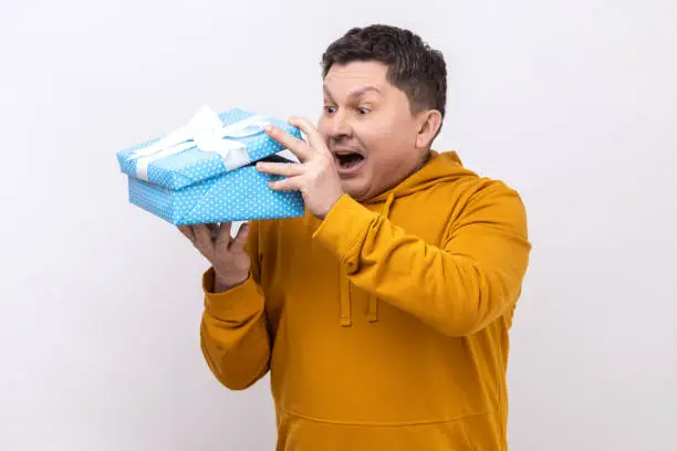 Photo of Curious middle aged man with present in hands looking inside gift box with surprised expression.