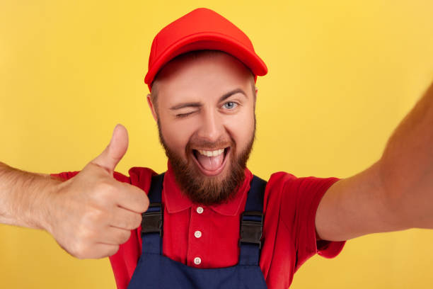 istock Smiling worker man wearing blue uniform taking selfie looking at camera winking and showing thumb up 1428532104