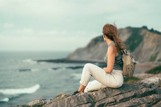 istock woman sitting on cliff looking towards the beach 1428534889