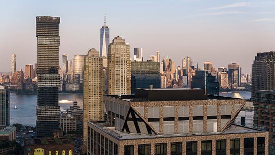 Jersey City Waterfront with the Exchange Place North modern skyscraper on green street. Remote view of Manhattan with famous Freedom Tower at sunset.