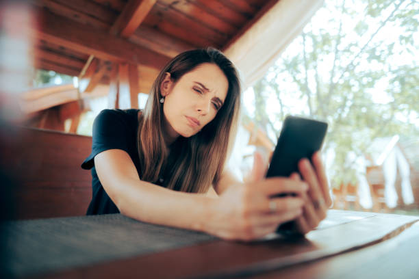 donna che strizza gli occhi cercando di leggere un piccolo testo sul suo telefono - strizzare gli occhi foto e immagini stock