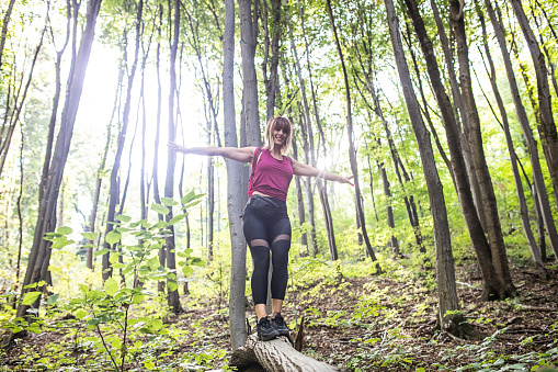Sporty woman balancing on a log, during her hike