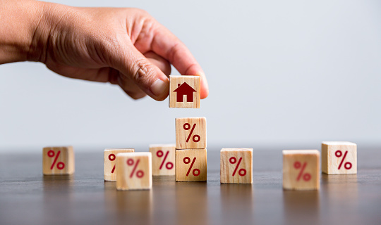 Hand building a house by wooden cubes with the percentage sign on them. Concept of Interest rate financial mortgage rates, home loans, home refinance, wooden block with percentage symbol and up arrow.