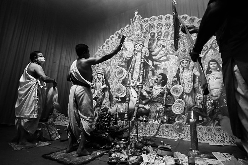 Howrah, India -October 13, 2021 : Hindu Priests worshipping Goddess Durga with Shari, ghanta, chamor and hand fan. Ashtami puja aarati - sacred Durga Puja ritual - shot at night.