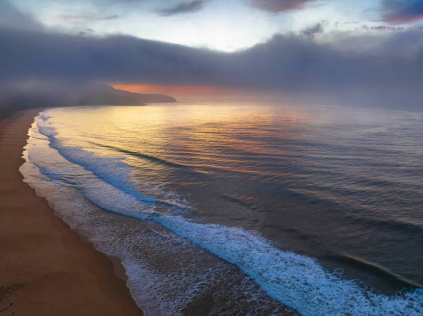 istock Peaceful sunrise over the ocean with small waves, clouds and fog rolling across 1428567146