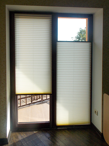 Pleated blinds closeup on the balcony door in a private house. Cordless pleated shades. Modern top down bottom up privacy cellular shades on apartment window.
