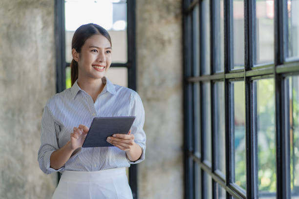 Confident and creative Asian businesswoman using tablet smiling female executive manager secretary offering professional business services holding digital tablet standing in office