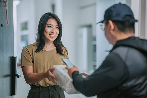 Asian Chinese woman receiving delivery package signing receipt of home delivery on smart phone
