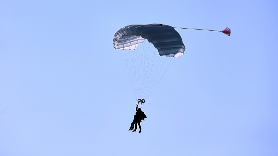 A skydiver with a white parachute canopy against a blue sky and white clouds, close-up.