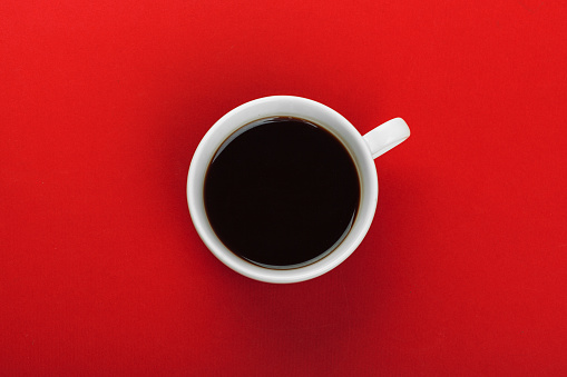 Coffee cup with coffee beans on red background.