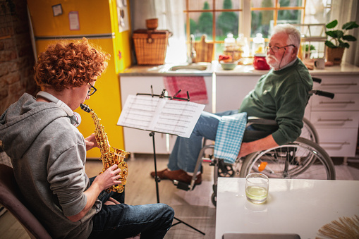 Happy senior man and grandson having fun while playing saxophone at home