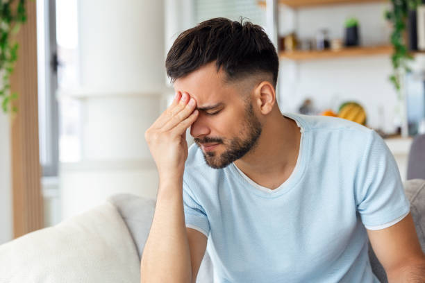 istock Feeling stressed. Frustrated handsome young man touching his head and keeping eyes closed while sitting on the couch at home 1428595607