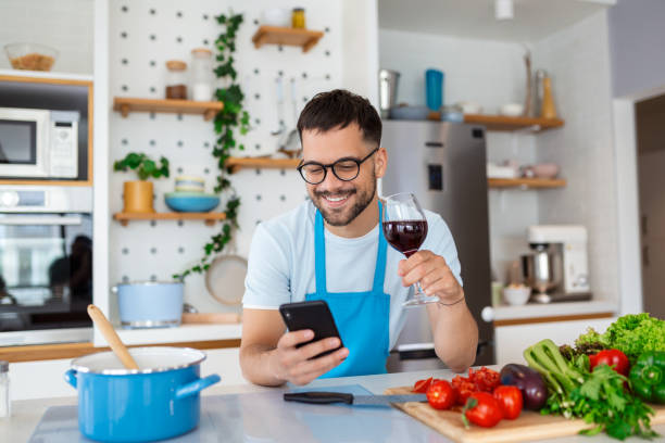 istock Head shot smiling young man using smartphone, chatting in social network while preparing food for vegetarian dinner at home. Happy millennial guy in eyeglasses web surfing recipe for meal in kitchen. 1428595627