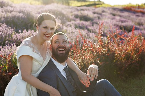 Portrait of happy just married couple sitting and hugging in lavender field