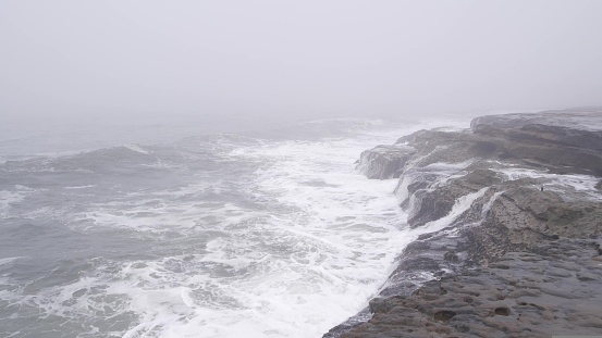 Foggy sea landscape, waves crashing on ocean beach in haze, misty weather. Calm tranquil moody atmosphere, grey monochrome seascape, gloomy dramatic shore cliffs or coast rocks. stormy water surface.