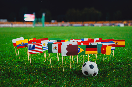 National flags of Qatar, Brazil, Germany, USA and other football countries on green grass of Stadium in night. Soccer ball, black background