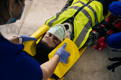 Employee accident in construction site work. Team EMS Paramedic first aid apply hard collar and spinal board support builder neck and head injury from accident in site work. First aid procedure.