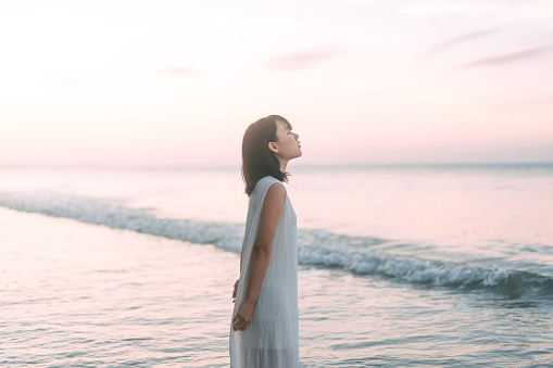 Portrait of asian woman at the beach rest in the sea waves aesthetic vibes. People relax in nature concept.