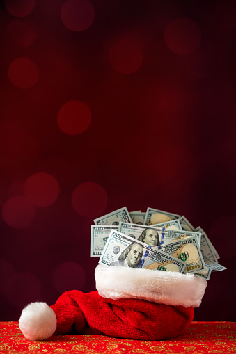 Red Santa hat full of US $100 dollar bills. Defocused lights (bokeh) background, space for copy.