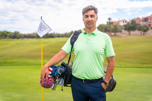 Portrait of a man playing golf together with the clubs on the green, enjoying the sport