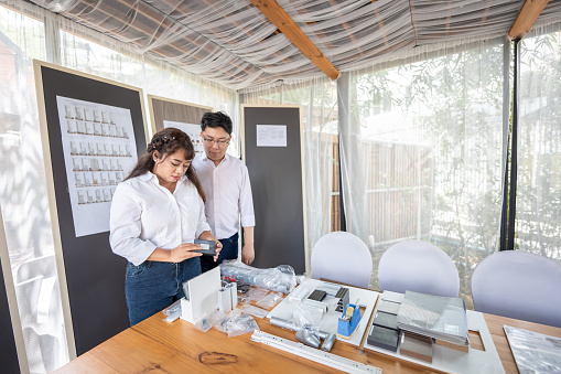 Asian Man and woman are choosing materials for interior decorations placed on a brown wooden table.