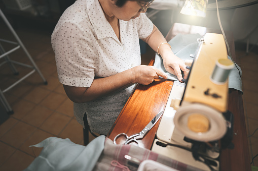 Retirement tailor southeast asian elderly crafting a cloth by sewing machine. Baby boomer generation mature working at home concept. Life moments in candid portrait authentic people.