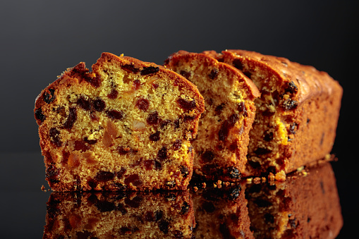 Cake with raisins and candied fruit on a black reflective background.