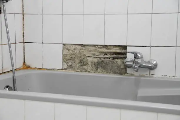 Photo of An old bathroom with broken white tiles and mold