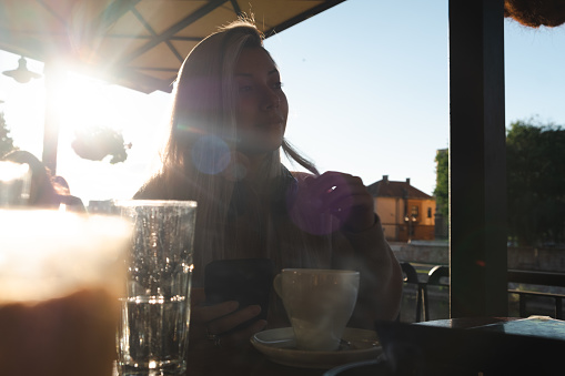 Young blonde woman portrait in a cafe garden at sunset
