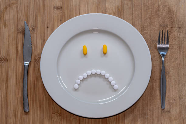 Pills on the plate in the shape of miserable and unhappy face, healthcare, dieting or taking medication concept Top view of plate with various pills arranged in the shape of sad face diet pills stock pictures, royalty-free photos & images