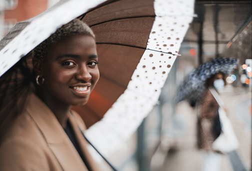 A true tilt-shift portrait with a selective focus on the part of the face of a cute cheerful young black female with a wet spotted umbrella waiting at the bus station on a rainy autumn day