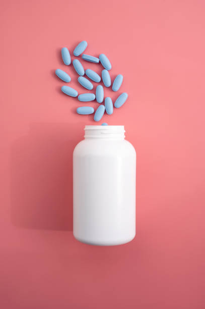 青い丸薬、ビタミン、または食品のしなやかさが入った白いペットボトル。ピンクの背景に薬の丸薬が入�った空の容器。 - capsule pill white nutritional supplement ストックフォトと画像