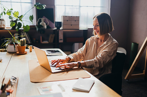 A smiling Caucasian entrepreneur working online using her laptop.