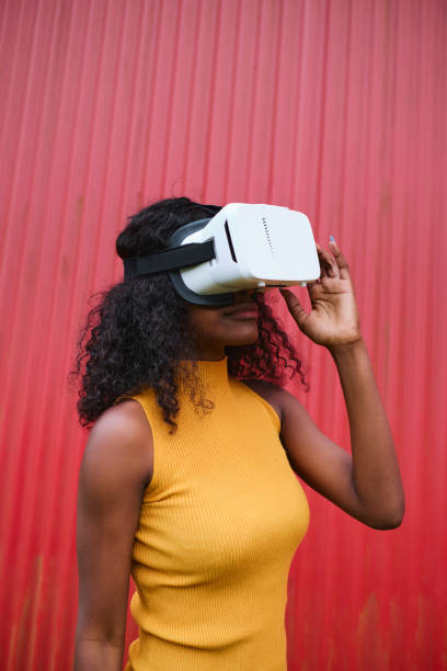istock Young woman standing using vr goggles outdoors on a red background 1428640215